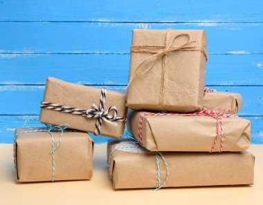 Kahverengi kraft kağıdına sarılı ve iple bağlanmış bir yığın hediye. Mavi arka planda kutular.