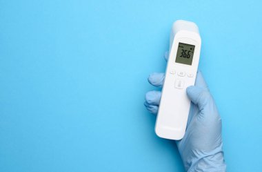 Mavi lateks eldivenler, sıcaklığı ölçmek için elektronik termometreyi tutar. Temassız cihaz, sıcaklık 36.6 dereceyi gösterir. 