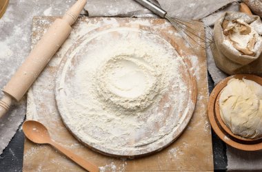 Yuvarlak ahşap bir tahtanın üzerine istiflenmiş beyaz buğday unu, ahşap bir tabakla yoğurulmuş hamur, üst manzara.