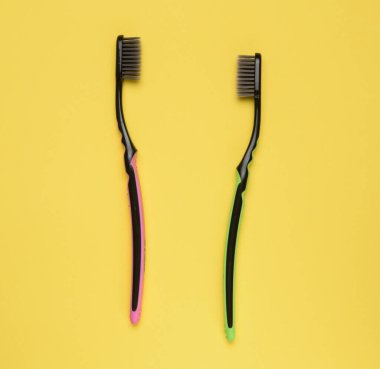 Sarı arka planda pembe ve yeşil plastik diş fırçaları, üst manzara.