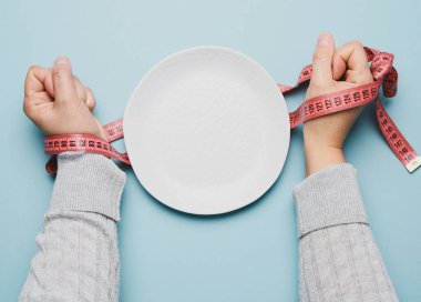 Beyaz yuvarlak bir seramik tabakta kırmızı bant ile bağlanmış iki kadın eli, ince bir konsept, üst görünüm