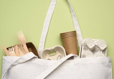 Beyaz tekstil çantası ve yeşil arka plandaki kahverengi el işi kağıttan tek kullanımlık sofra takımı. Yukarıdan görünüm, plastik reddetme konsepti, sıfır atık 