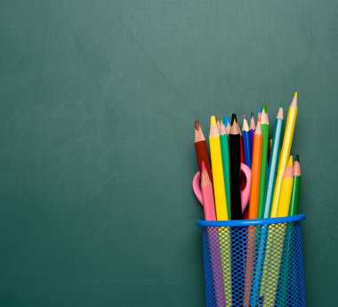 Çok renkli tahta kalemleri ve kalemleri olan mavi kırtasiye camı, karatahta arka planı, kopyalama alanı