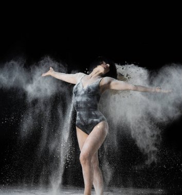 Güzel beyaz kadın elleri farklı yönlere doğru beyaz un fırlatıyor siyah arka planda, zarif bir dans.