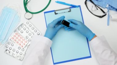 Doktorun elinde elektronik nabız oksimetresi, mavi lateks eldivenler, doktorun masasının üst görüntüsü.