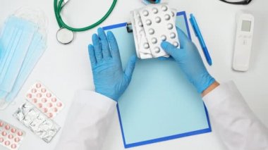 Doktorun beyaz çalışma masasının üst görüntüsü, doktor bir yığın hapı su toplamış, sol eliyle hareket ediyor, sohbet ediyor.