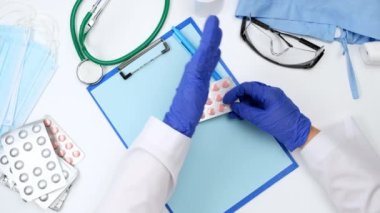 Doktorun beyaz çalışma masasının üst görüntüsü, doktor bir yığın hapı su toplamış, sol eliyle hareket ediyor, sohbet ediyor.