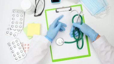 Beyaz önlüklü ve mavi lateks eldivenli doktor tıbbi bir steteskop tutuyor, sol eliyle jestler yapıyor, doktorun iş yerini görüyor.