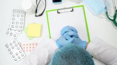 Başında mavi lateks eldiven ve tek kullanımlık koruyucu başlık olan doktor masasının en üst görüntüsü.