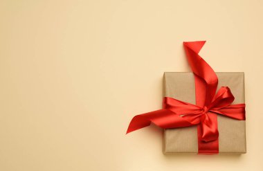 Kare hediye kutusu kırmızı kağıt ve kıvrımlı ipek kurdeleyle paketlenmiştir, şenlikli arka plan, üst görünüm 