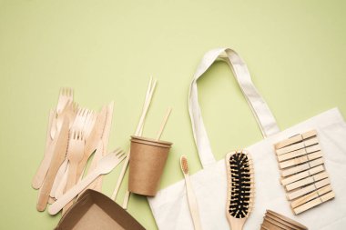 Beyaz tekstil çantası ve yeşil arka plandaki kahverengi el işi kağıttan tek kullanımlık sofra takımı. Yukarıdan görünüm, plastik reddetme konsepti, sıfır atık 