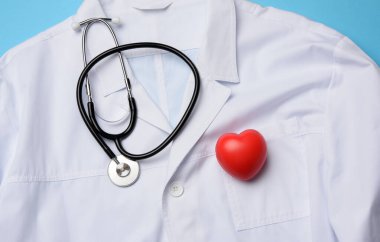 Kırmızı kalp ve siyah steteskop beyaz bir medikal elbisenin üzerinde yatıyor.