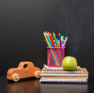 Defter, pembe kırtasiye camı, arka planda çok renkli tahta kalemler, boş bir tebeşir tahtası, okula dönüş konsepti.