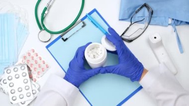 Beyaz önlüklü doktor ve mavi lateks eldivenler plastik bir kavanozdan beyaz haplar döküyor.