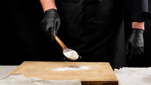黒の制服と黒のラテックスの手袋のシェフは白い小麦粉と木製のスプーンを保持しています — ストック動画