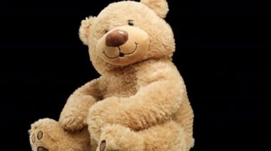 Gülümseyen büyük kahverengi ayıcık siyah bir arka planda dönüyor, çocuk oyuncağı.