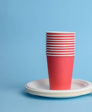 Kırmızı kağıt bardak, mavi arka planda beyaz tabaklar. Plastik reddetme kavramı, sıfır atık, kopyalama alanı