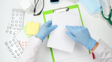 Doktorun iş yerinin üst görüntüsü, elinde beyaz bir kağıt tutarken, doktor çarşafı yırtıyor.