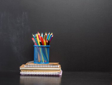 Defter, mavi kırtasiye camı, arka planda çok renkli tahta kalemler, boş bir tebeşir tahtası, okula dönüş konsepti.