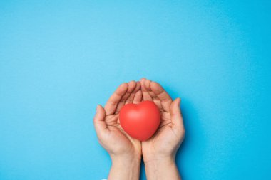 Kadın elleri kırmızı tekstil kalp, mavi arka plan. Sevgi ve bağışta bulunma konsepti.