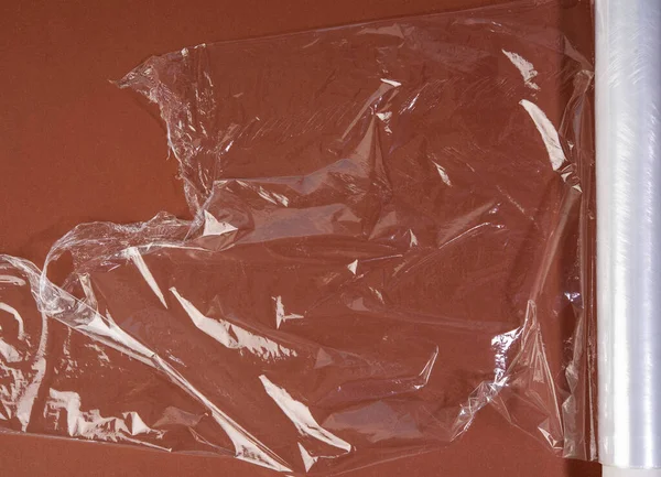 roll of transparent cling film for packaging on brown background, top view
