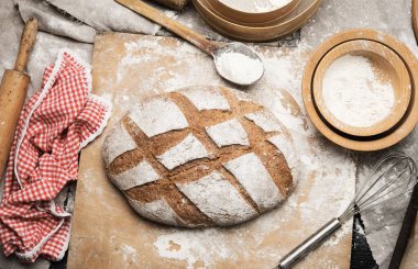 Masanın üzerinde bir somun ekmek ve malzemeler, mutfak gereçleri yakınlarda, üst tarafta.