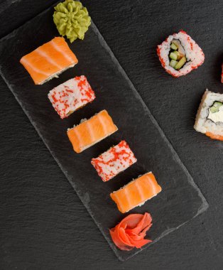 Kırmızı tobiko havyarlı Kaliforniya suşisi ve siyah tahtada Philadelphia suşisi dilimleri.