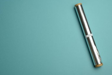 Mavi arkaplanda yemek pişirmek ve paketlemek için gri folyo rulosu, boşluğu kopyala