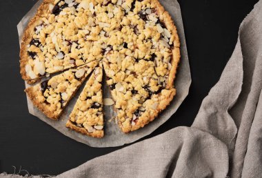 Kurutulmuş yuvarlak turta, erikli, siyah arka planda parçalara ayrılmış, üst görünümde.