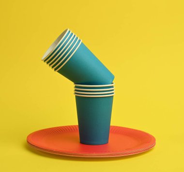 Mavi kağıt bardak, sarı arka planda kırmızı tabaklar. Plastik reddetme konsepti, sıfır atık