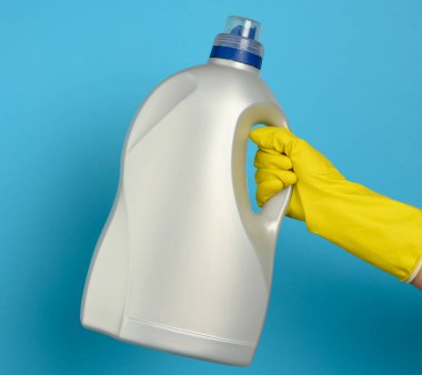 Mavi arka planda çamaşır yıkamak için sıvı deterjanı olan büyük bir şişeyi tutan el, kapat.