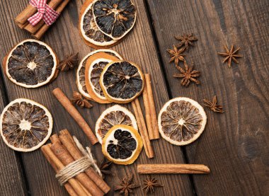 Kahverengi tahta üzerinde tarçın çubukları ve kuru portakal dilimleri, üst manzara.