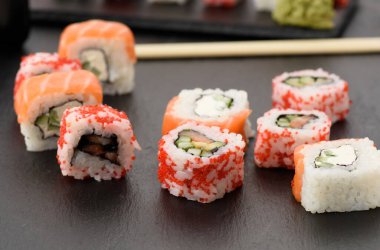 Kırmızı tobiko havyarlı Kaliforniya suşisi ve siyah tahtada Philadelphia suşisi dilimleri.