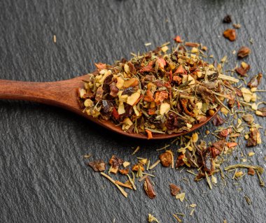 Ahşap bir kaşıkta çeşitli kurutulmuş baharatların karışımı, siyah arka plan, kapat.