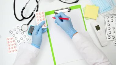 Doktorun beyaz çalışma masasının üst görüntüsü, doktor bir yığın hapı su toplamış, eliyle jestler, konuşmalar...