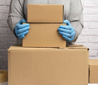  Gri kazaklı kadın valiz topluyor ve mavi eldivenler kahverengi karton kutular tutuyor, taşınıyor, bağış yapıyor. 