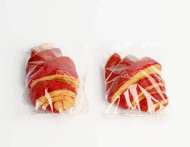 Şeffaf plastik bir torbaya kiraz jöleli kruvasan konmuş, beyaz arka plan, üst manzara.