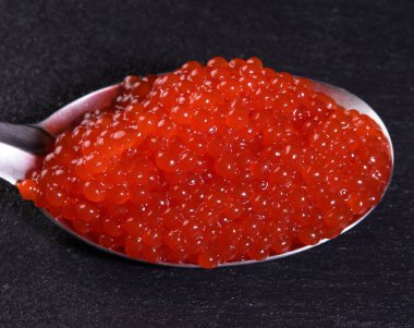 Siyah arka planda metal kaşıkta somon balığı kırmızı havyarı, yakın plan.
