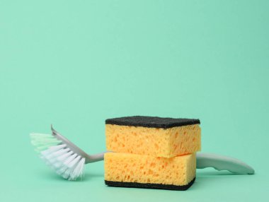 Bulaşık yıkamak için sarı mutfak süngeri ve yeşil arka planda plastik fırça.