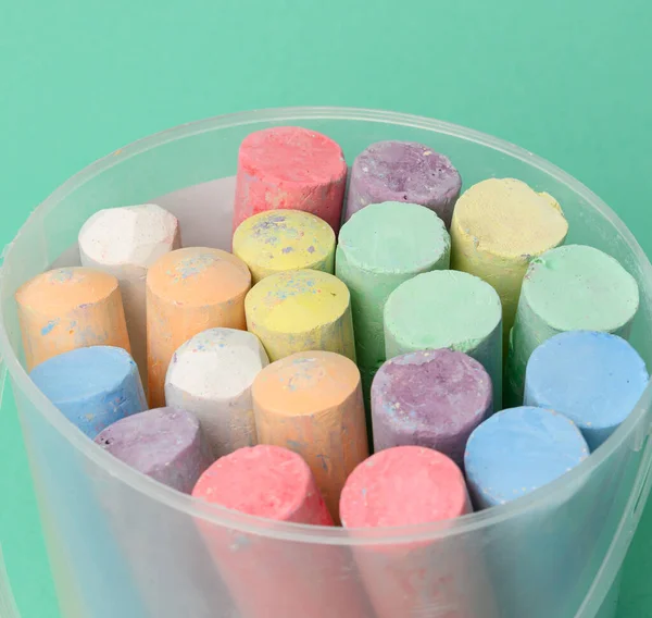 multicolored chalk in a plastic bucket on a green background, close up
