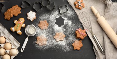 Yıldız şeklinde fırınlanmış zencefilli kurabiyeler üzerine pudra şekeri serpiştirilmiş siyah bir masa, üst manzara