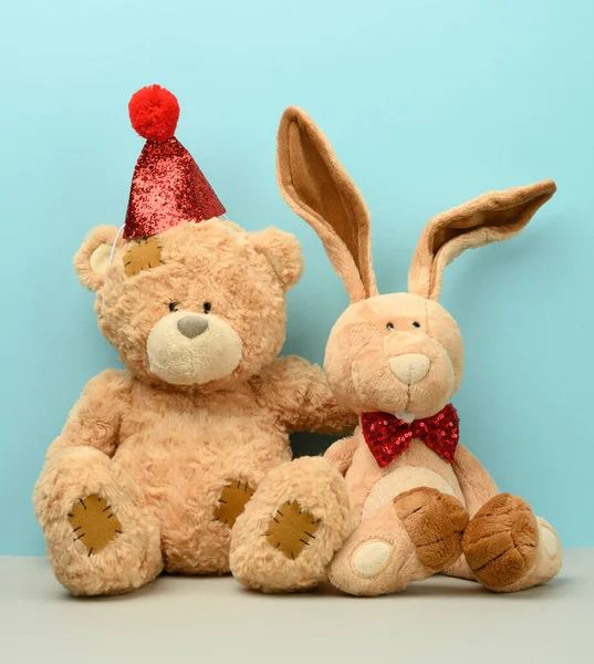 teddy bear in a cap and a cute teddy hare with long ears, a red butterfly is tied around the neck, blue background