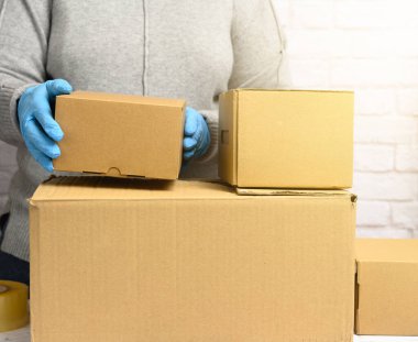  Gri kazaklı kadın valiz topluyor ve mavi eldivenler kahverengi karton kutular tutuyor, taşınıyor, bağış yapıyor. 