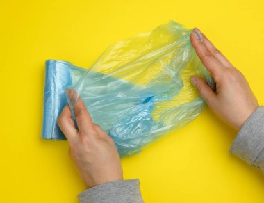 Kadın eli, çöp torbası, sarı arka plan, üst görünüm için mavi bir plastik poşet açar.