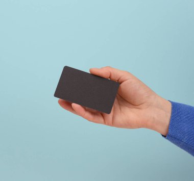 Kadın eli elinde siyah bir kartvizit, mavi arka plan, yakın plan.