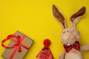 Pofuduk kahverengi tavşan, sarı arka planda bir kutuda hediye, üst manzara.