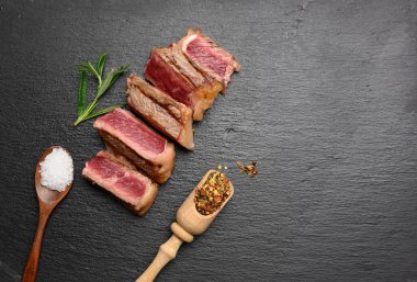 Dilimlenmiş biftek New York çizgili siyah arka planda baharatlı, az pişmiş, üst manzara, kopyalama alanı
