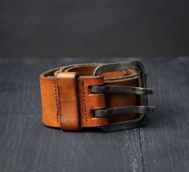 Kahverengi deri erkek kemeri, ahşap bir arka planda metal toka, yakın çekim.