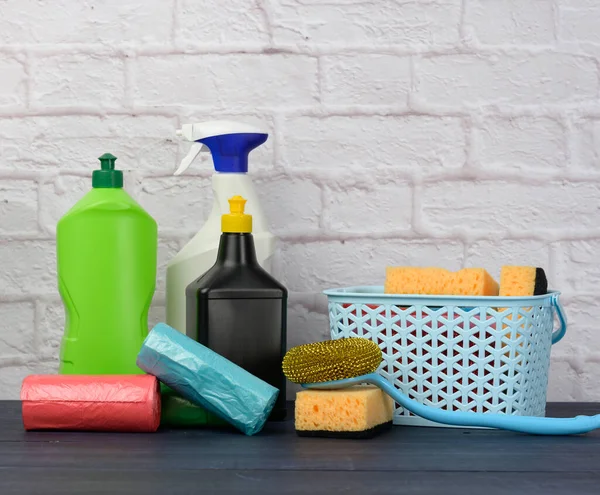 蓝色木制桌子上的海绵 塑料刷子和洗涤剂瓶子 白色砖墙背景上的家用清洁用品 — 图库照片