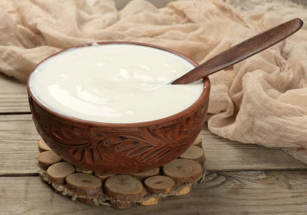 木制底座上有木勺的褐色陶瓷碗中的酸奶油 发酵过的牛奶有用的产品 顶部视图 — 图库照片